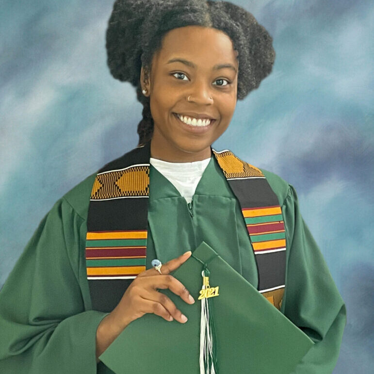 A woman in green graduation gown and holding her diploma.